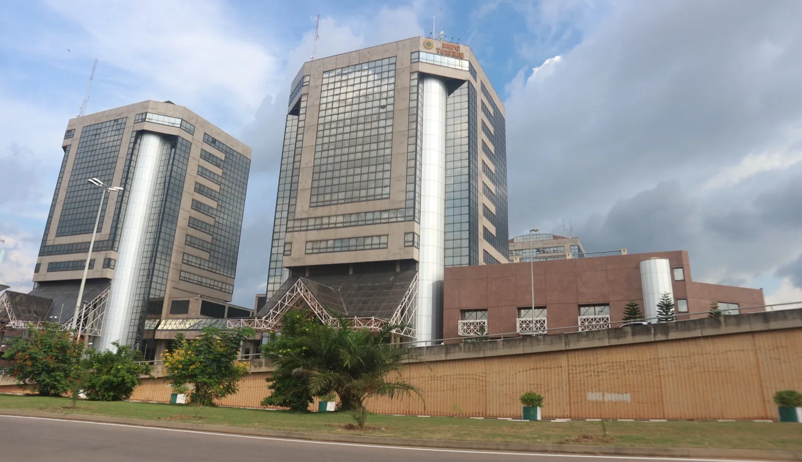 A compliance listing of company names with filing status flags beside a stock exchange trading board.