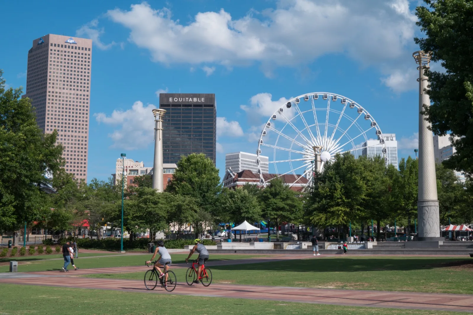 Cyclists passing through Centennial Olympic Park with downtown Atlanta skyline in the background